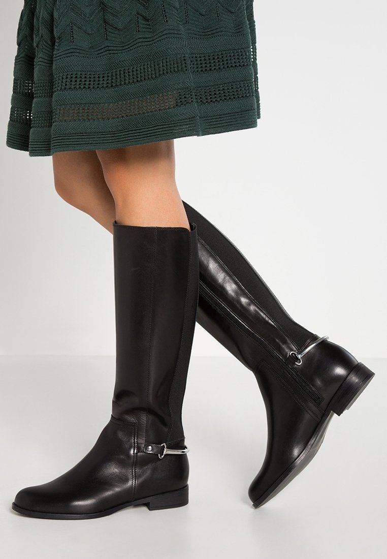 Bottes noires en cuir jusqu'au genou avec une finition lisse, dotées d'une fermeture éclair latérale et d'une sangle argentée autour de la cheville.