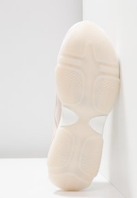 Obuv s světlou růžovou textilní svrškem, s hladkým povrchem a texturovanou bílou gumovou podešví, která má vlnitý vzorek.