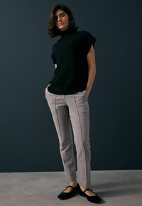 Černý pletený svetr s krátkým rukávem, šedé kostkované slim-fit kalhoty s bočními pruhy a černé baleríny na tmavě modrém pozadí.