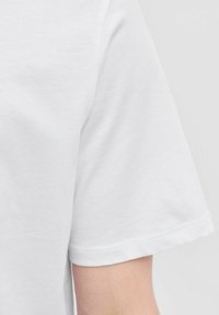 Weißes Baumwoll-T-Shirt mit Rundhalsausschnitt und kurzen Ärmeln. Glatte Textur, gesäumte Ärmel und leicht lockere Passform.