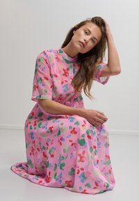 Blommönstrad rosa klänning av lättviktsmaterial. Har en krage, korta ärmar och knappar fram. Slät textur.