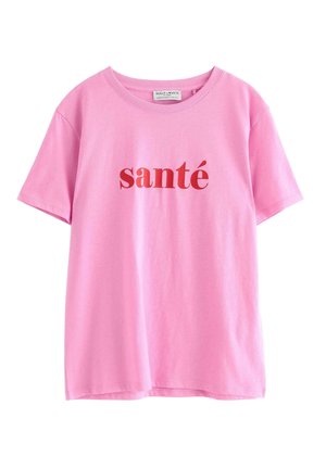 Vaaleanpunainen puuvillapaita, jossa on pyöreä kaula-aukko ja lyhyet hihat. Paidassa on rintaosassa rohkealla punaisella fontilla tulostettu sana "santé".