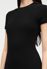 Μαύρο φόρεμα με υφή από ριγέ, πιετά ύφασμα, με κοντά μανίκια και στρογγυλή λαιμόκοψη. Λείο ύφασμα, εφαρμοστή σιλουέτα, ελάχιστες λεπτομέρειες.