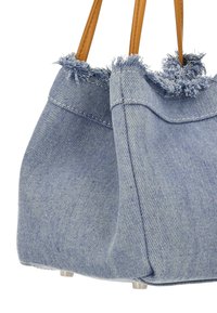 Denim draagtas met rafelige randen, lichtblauwe kleur en handvatten van bruin leer. Kenmerkt zich door een gestructureerde vorm en kleine metalen pootjes aan de onderkant.