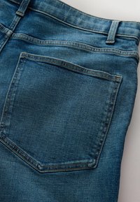 Vue arrière d'un jean en denim bleu montrant une seule poche arrière avec des surpiqûres visibles et une boucle de ceinture sur un fond clair.