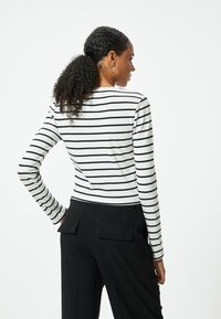 Lange mouwen, witte en zwarte gestreepte top met een ronde hals. Gecombineerd met hoge zwarte broeken met twee achterzakken.