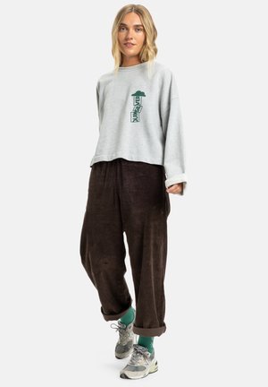 Sweatshirt gris court avec graphique vert, associé à un pantalon en velours côtelé marron. La tenue inclut des sneakers gris et vert avec les ourlets retroussés.