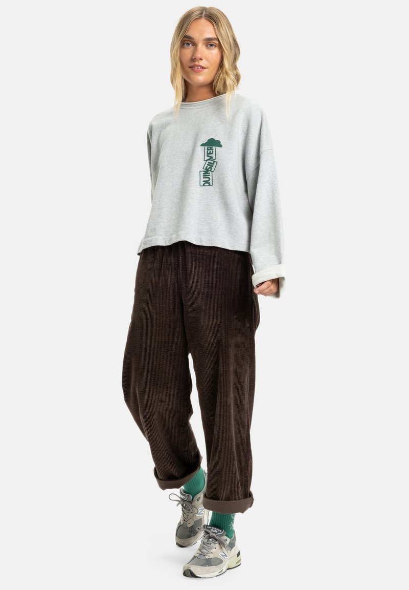 Sweatshirt gris court avec graphique vert, associé à un pantalon en velours côtelé marron. La tenue inclut des sneakers gris et vert avec les ourlets retroussés.