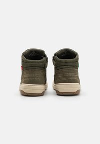 Botas con un upper de ante verde oscuro, textura de malla en el cuello, suela beige y cremalleras a ambos lados. Se aprecian acentos rojos y verdes.