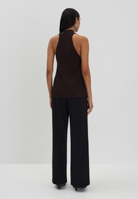 Top senza maniche marrone con collo alto, abbinato a pantaloni neri a gamba larga. Il tessuto sembra liscio con un design aderente.