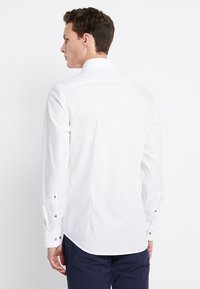 Weißes Langarmshirt mit geradem Schnitt, Knopfmanschetten und klassischem Kragen. Glatte Textur, minimales Design und keine sichtbaren Muster.
