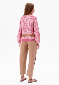 Roze trui met witte zebra-strepen, ballonmouwen en een gradient bruine zoom, gecombineerd met beige loszittende broeken en bruine sandalen.