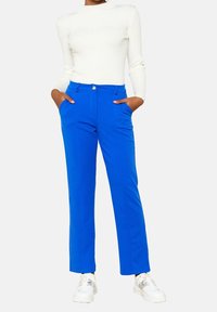 Blå skräddarsydda byxor med smal passform, två sidofickor och knappstängning. Kombinerade med en vit ribbad långärmad top och vita sneakers.