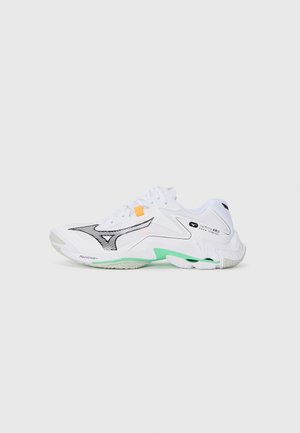 White athletic shoe with black accents, a green sole, and a textured design. Features mesh panels and a prominent logo on the side.