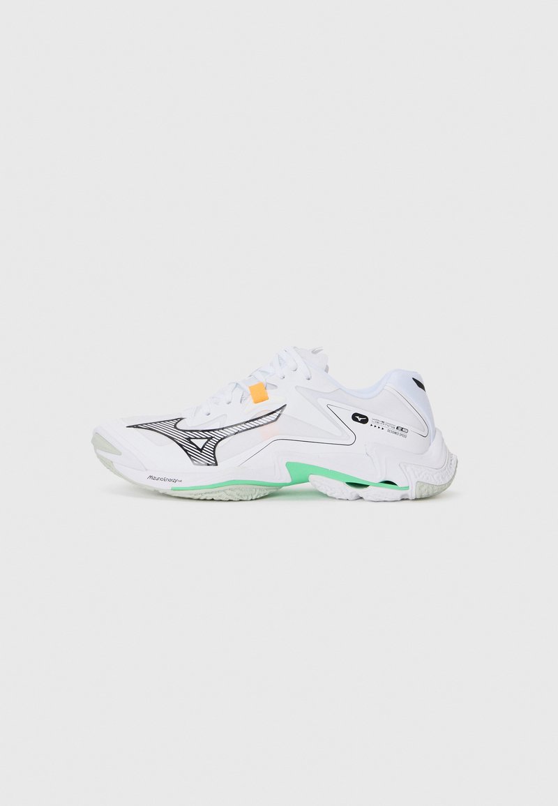 Weißer Sportschuh mit schwarzen Akzenten, einer grünen Sohle und einem strukturierten Design. Verfügt über Netzpaneele und ein auffälliges Logo an der Seite.