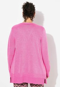 Cardigan long rose en tricot texturé, avec des fentes latérales et un ourlet côtelé. La vue de dos montre une coupe ample et décontractée.