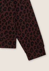 Manche de pull marron ornée d'un imprimé léopard noir. Le tissu est doux et extensible avec un poignet ajusté à l'extrémité. Le nom de la marque "FREDDY" est brodé.