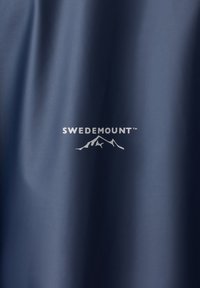 Blåt stof med "Swedemount" mærkenavn og logo med stiliseret bjerg- og fuglemotiv i hvidt.