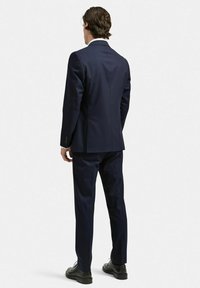 Marineblå kostym med skräddarsydd design, två bakventiler och en smal passform. Högkvalitativt tyg med en mjuk yta, kombinerat med svarta skor.