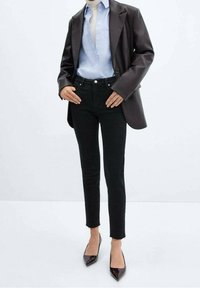 Jeans skinny negros con dobladillo deshilachado, combinados con una camisa de botones azul claro y un abrigo oscuro de gran tamaño. Completado con tacones de charol puntiagudos.