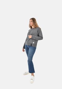 Maglione grigio a maniche lunghe con una vestibilità rilassata e spacchi laterali, abbinato a jeans blu a zampa d'elefante e sneakers bianche. Tessuto texturizzato con etichetta logo.