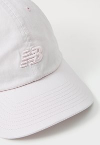 Lyserød baseballcap lavet af bomuld, med et broderet New Balance-logo på fronten, rund skygge og synlige stikninger.