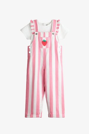 Balta īsroku krekls zem rozā un baltām vertikālām svītrainām pārvalkiem ar krokojumu lencēm un priekšēju kabatu ar sarkanas zemenes dizainu.