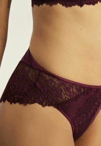 Bordowe koronkowe bielizna z gładkim pasem w talii i misternymi koronkowymi detalami wzdłuż krawędzi, z kwiatowym wzorem.