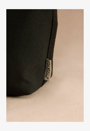 Czarna torba tekstylna o fakturowanej powierzchni i widocznej metce. Projekt charakteryzuje się prostymi liniami i lekko zakrzywionym dnem.