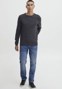 Suéter de punto gris oscuro con cuello redondo, combinado con jeans de mezclilla azul claro y zapatillas negras. Diseño sencillo y corte ajustado.