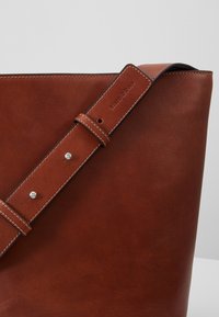 Sac cabas en cuir marron avec bandoulière réglable, clous argentés et branding embossé Marc O'Polo.