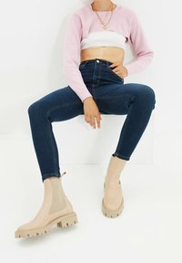Botines beige hasta el tobillo con paneles texturizados, suela gruesa y tirador trasero, combinados con jeans skinny oscuros y un suéter corto rosa.