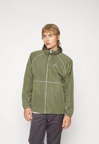 Olive green lightweight jacket with a hood, zip closure, and white accents. Features elastic cuffs and a minimal logo on the chest.