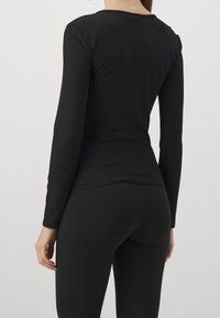 Top nero a maniche lunghe con texture a coste, caratterizzato da un collo rotondo e una vestibilità aderente, abbinato a leggings neri coordinati.