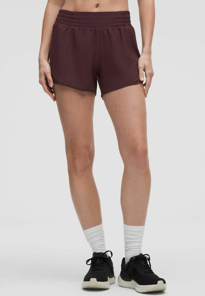 Vinröda sportshorts med en texturerad midja, kort skärning och slätt tyg. Kombineras med svarta sneakers och vita sockor.