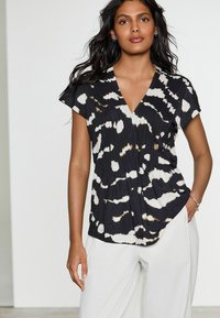 Blusa a rayas en blanco y negro con escote en V, mangas cortas y textura plisada. Combinada con pantalones blancos de corte relajado.