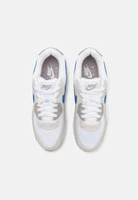 Sapatilhas Nike Air com um cabedal predominantemente branco, detalhes em cinza e azul, painéis em malha e atacadores brancos planos.