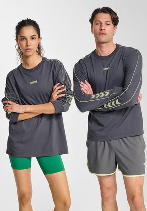 Chemises à manches longues gris foncé avec des accents vert clair ; un modèle portant un short vert et un autre modèle en short gris avec une décoration similaire.