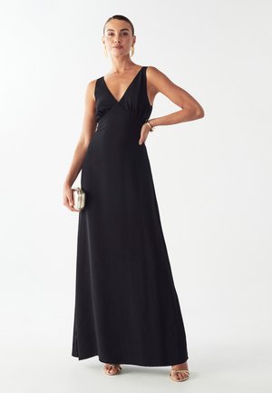 Schwarzes Maxikleid mit einem tiefen V-Ausschnitt, figurbetontem Oberteil und fließendem Rock. Geschmeidiger Stoff mit eleganter Drapierung. Kombiniert mit goldenen Akzenten und Accessoires.