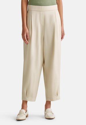 Pantalones palazzo beige con una textura suave, que presentan pliegues frontales y un diseño de cintura media. Combinados con mocasines de color claro.