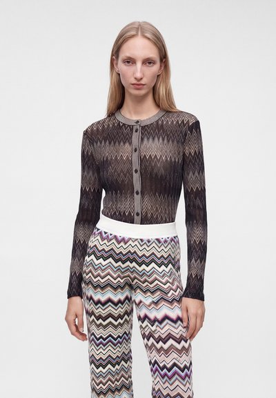 Femme portant un cardigan à manches longues noir et beige à motif zigzag et un pantalon taille haute multicolore à motif zigzag.