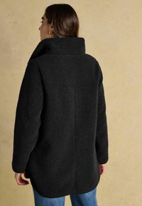 Mustat fleecetakki, jossa on korkea kaulus, texturoitu pinta ja lasketut olkapäät. Ominaisuuksiin kuuluu suora leikkaus ja sivuhalkiot helmassa.