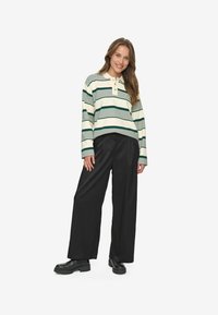 Polo a maniche lunghe a righe con strisce crema e verde scuro, dotato di una patta con bottoni. Abbinato a pantaloni neri larghi e stivali neri robusti.