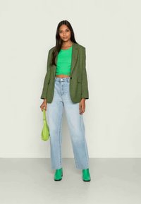 Zaļš hounds-tooth modelis žakete virs pieguļošā zaļā sporta krekla, saskaņota ar gaiši ziliem augstās jostasvietas džinsiem un zaļām potīšu zābakām; tur zaļu somu.