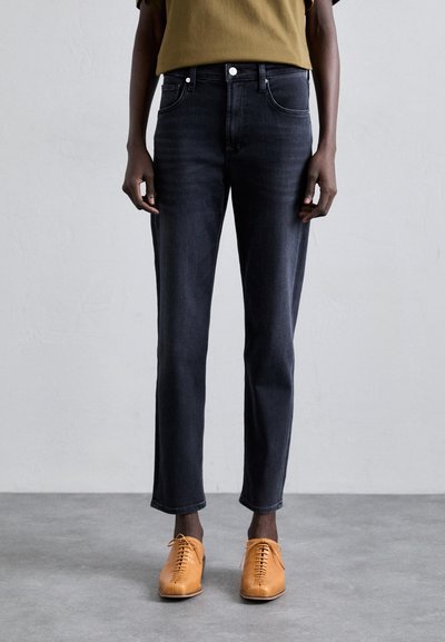 Jeans din denim închis cu picior tapered, având buzunare frontale și închidere cu nasture. Asortați cu pantofi de culoare albăstrie deschis, cu șireturi.