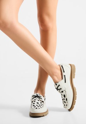 Hvide sko med sort dalmatinerprint, strukturerede snørebånd og gummisål. Designet har spids tå og let hævet hæl.