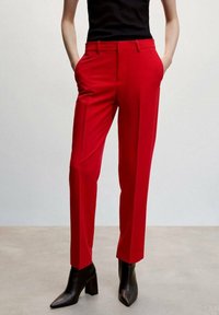 Pantalons ajustés rouges à coupe droite, avec poches latérales et un tissu lisse. Associés à des bottines à talons aiguilles noires.
