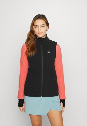 Chaleco negro con cierre y cuello alto, combinado con mangas largas rosas. La modelo lleva una falda-pantalón azul, mostrando texturas suaves y colores contrastantes.