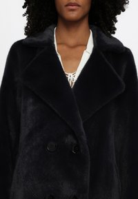 Navy double-breasted coat with a fluffy texture, wide notched collar, and black buttons. Lined with a lighter shade beneath the collar.