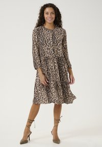 Rochie cu imprimeu leopard maro, cu mâneci lungi, guler rotund și un design în straturi. Asortată cu sandale cu toc înalt, verzi măslinii, cu barete.